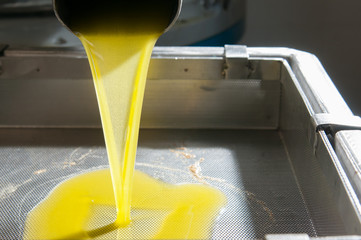 Olive oil running from a steel pipe into a metal decanter inside an oil mill