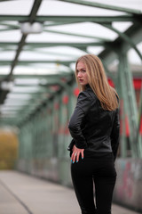 Beautiful blonde woman in leather jacket and leggings on a bridge