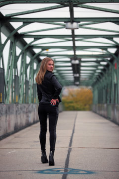 Beautiful blonde woman in leather jacket and leggings on a bridge