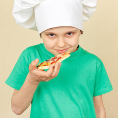 Little boy in chefs hat is going to try a cooked pizza