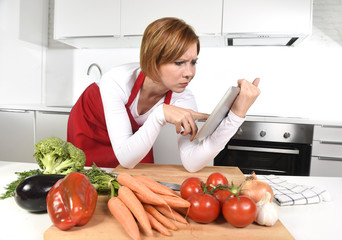 inexperienced home cook woman in apron at kitchen using digital tablet as recipe reference