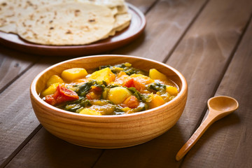 Pumpkin, mangold, potato and tomato curry dish with homemade chapati flatbread in the back photographed with natural light (Selective Focus, Focus in the middle of the curry dish)