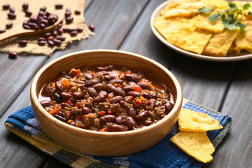 Chili con carne with homemade tortilla chips in the back, photographed with natural light (Selective Focus, Focus in the middle of the chili)