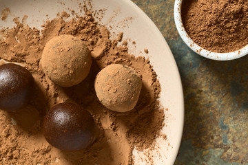 Rum balls being covered with cocoa powder, photographed overhead on slate with natural light (Selective Focus, Focus on the top of the balls)