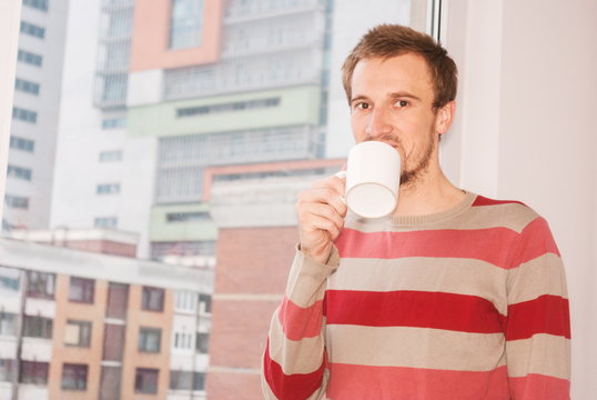 Young man drinking coffee and looking through the window