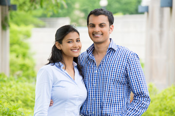 Closeup portrait, attractive wealthy successful couple in blue shirt and striped outfit holding each other smiling, isolated outside green trees background.