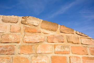 Sandstone brick wall and blue sky, bathed in afternoon sun 
