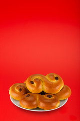 Swedish saffron bun, called "lussekatt" in Sweden, on a white plate on red background. Copy space for text etc.