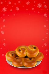 Swedish saffron bun, called "lussekatt" in Swedish, on a white plate on red background with scattered snowflakes. Copy space for text etc.