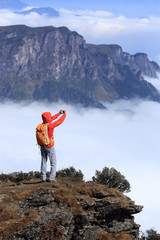 young asian woman backpacker taking photo with smartphone on mountain peak
