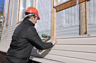 A worker installs panels beige siding on the facade - obrazy, fototapety, plakaty