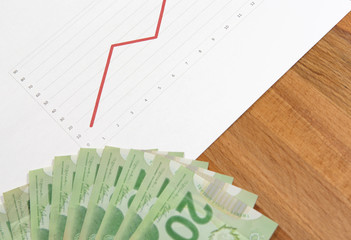 Stock market going up. An image with a pile of cash next to a paper sheet showing the red line as values.