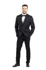 Laughing happy young man in tuxedo with bow tie looking at camera. Full body length portrait isolated over white studio background.