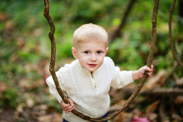 child boy in a bright sweater with lianas in the forest