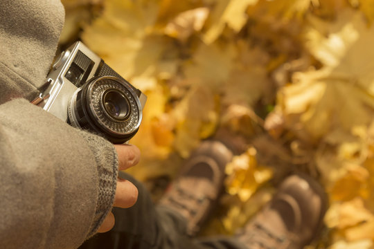 Female holding retro camera and standing on yellow leaves covered ground