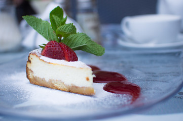 Piece of cheesecake with strawberry and mint leaf, out of focus