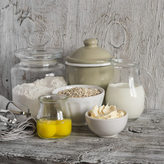 Ingredients for baking - flour, milk, butter, eggs on a light wooden table.