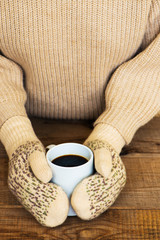Woman hands in teal gloves are holding a mug with hot coffee or