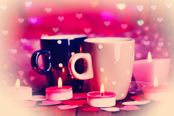 Two cups and candles on table on bright lights background