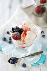 Delicious ice cream with fresh frozen berries and sauce, on color wooden background