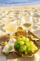 Fototapeta premium Romantic composition of white wine and grape on sandy beach