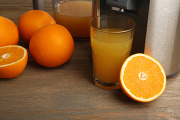 Stainless juice extractor with glass of orange juice on wooden background, close up