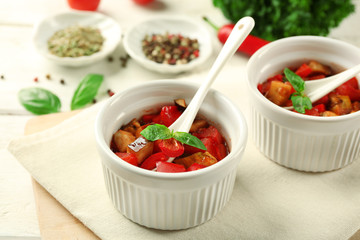 Tasty vegetarian ratatouille made of eggplants, squash, tomatoes in bowls on wooden table background