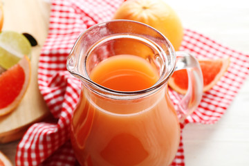Jar of citrus juice and fresh fruits on light wooden background