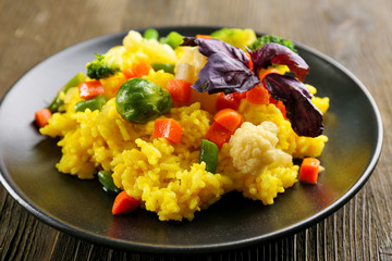 Rice with vegetables on black plate on wooden background
