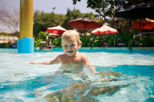 small blonde girl plays smiles in transparent water of pool