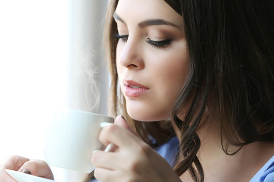 Woman drinking coffee near window in the room