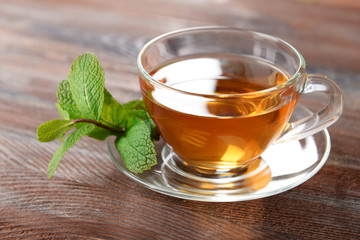 Glass cup of tea with mint leaves on wooden background