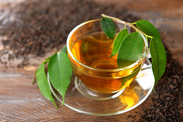 Glass cup of tea with green leaves on wooden background decorated with scattered tea