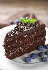 Chocolate cake with chocolate cream and fresh blueberries on plate, on wooden background
