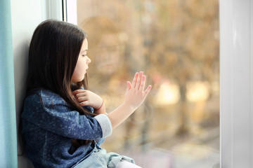 Little girl waiting for someone and looking out the window