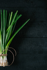 Bunch of green young scallions with roots on a black background of the old wooden boards vintage top view