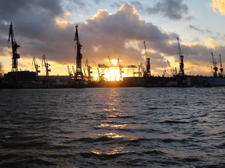 Naklejka premium Sonnenuntergang am Hamburger Hafen, die Sonne versinkt hinter den Hafenkranen