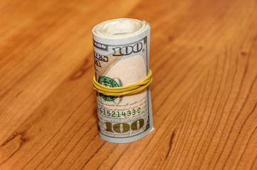 American one hundred Dollar Bills rolled up on the wood backgrou