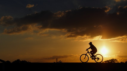 Fototapeta na wymiar A woman rides a bicycle on the road when sunset: silhouette photo