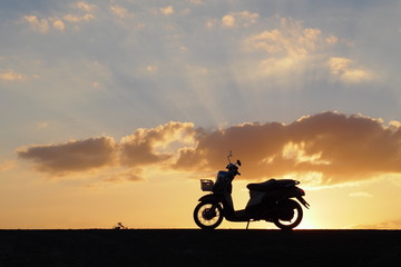 Obraz na płótnie Canvas A motorbike on a road in the evening: silhouette photo