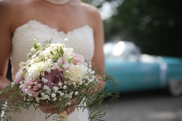 Braut mit Brautstrauß vor Hochzeitsauto