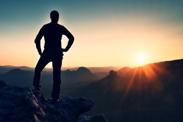 Man stands on the peak of sandstone rock in national park Saxony Switzerland and watching to Sun. Beautiful moment the miracle of nature