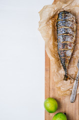 Baked fish with lime on parchment paper and cutting board on a white background of the old wooden boards vintage top view vertical
