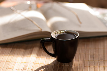 cup of coffee, standing next to an open book, on which lie glass