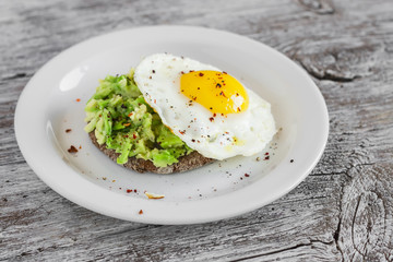 sandwich with avocado and a fried egg on a white plate on a light rustic wood surface