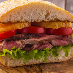 Juicy steak sandwich with vegetables and slices of orange.