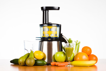Slow juicer with fruit, vegetables and a glass of fresh juice on wooden table with white...