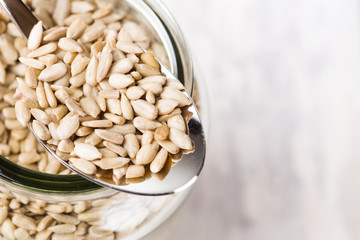 sunflower seeds in a metal spoon on a jar filled with sunflower seeds, top view. The jar is on a white wooden vintage table. Space for copy text. Selective focus.