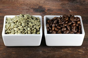 geröstete und ungeröstete Kaffeebohnen in weißen Keramikschalen auf Holzhintergrund
