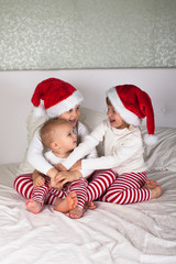 funny kids in their pajamas and Christmas caps on the bed